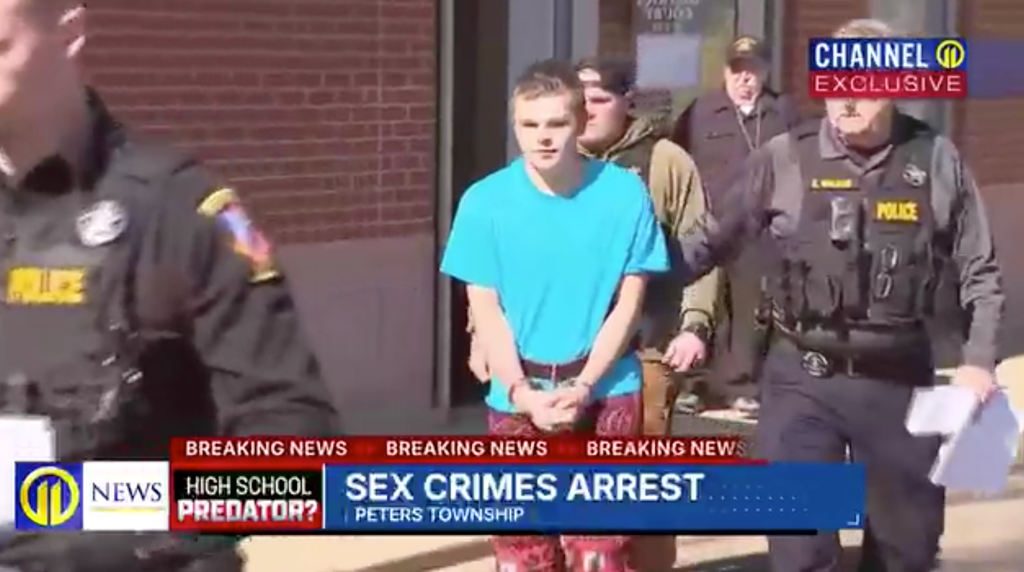 A young man in a blue shirt and patterned pants, handcuffed, being led by police officers, with news headlines 